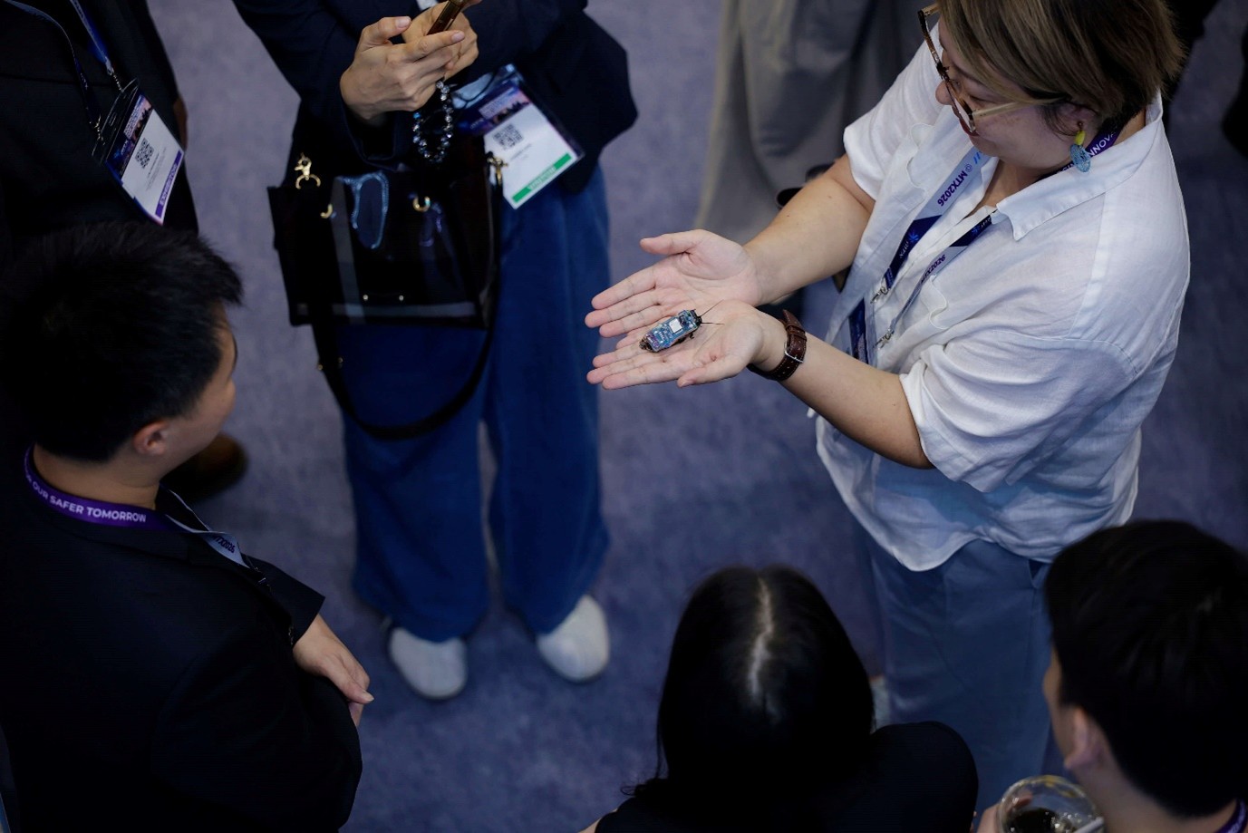 Group of people standing in a circle, with one person holding a live cyborg cockroach.