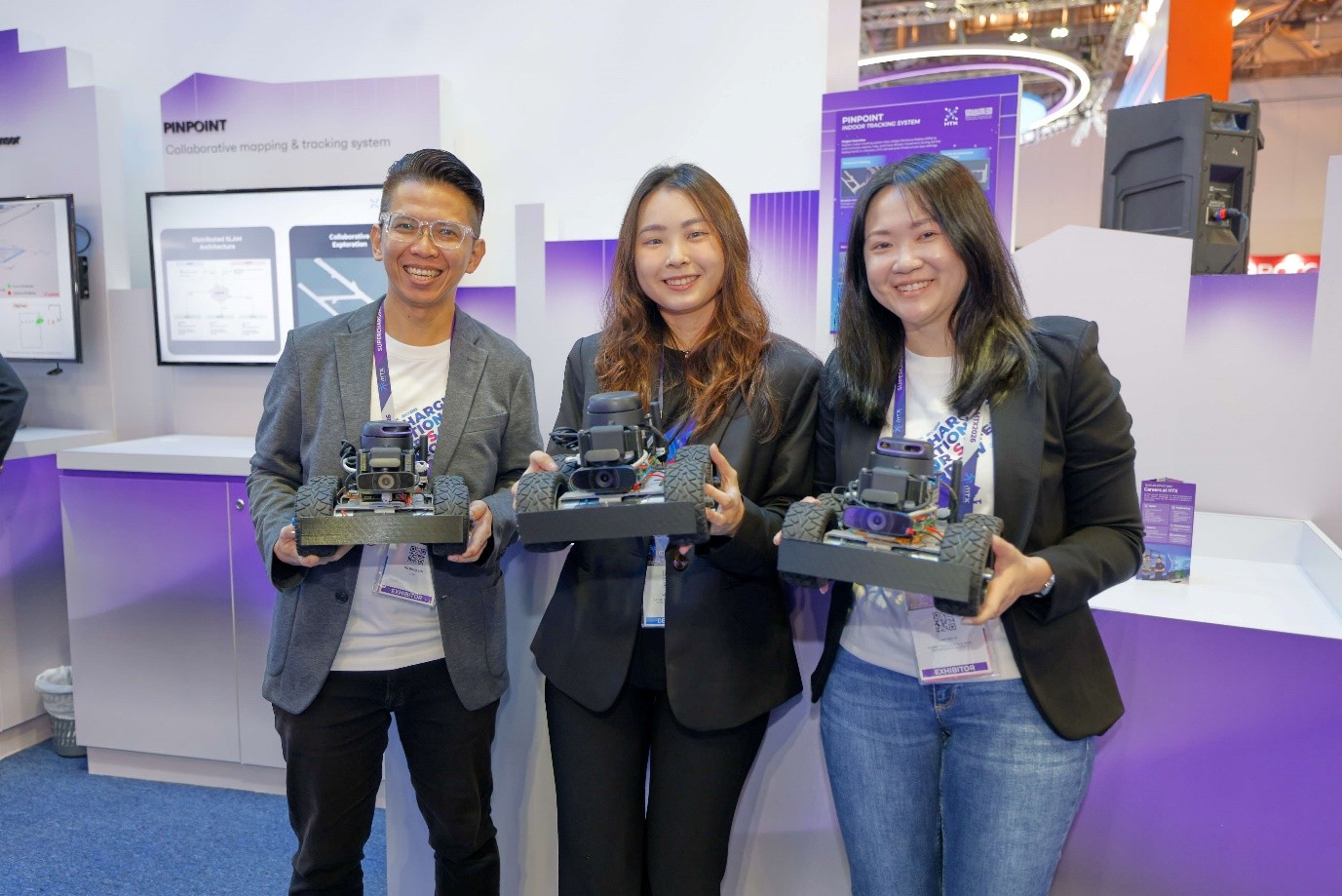 Three people holding a robotic system each at a tech booth.